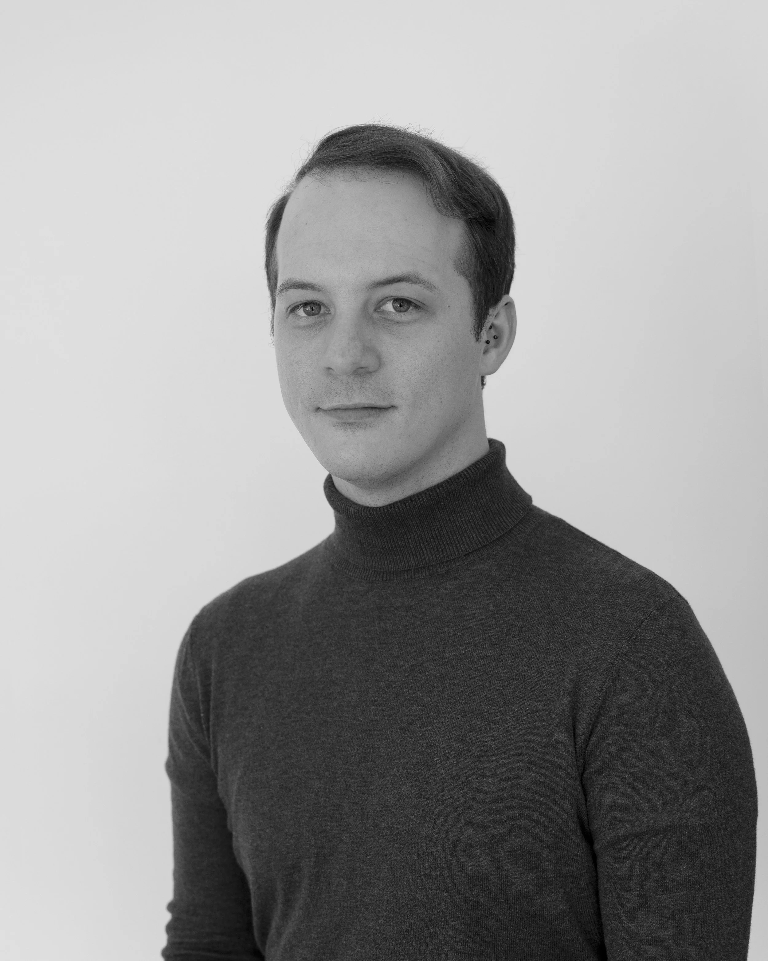 A black and white portrait of a person with short hair wearing a turtleneck sweater, looking slightly to the side against a light background.