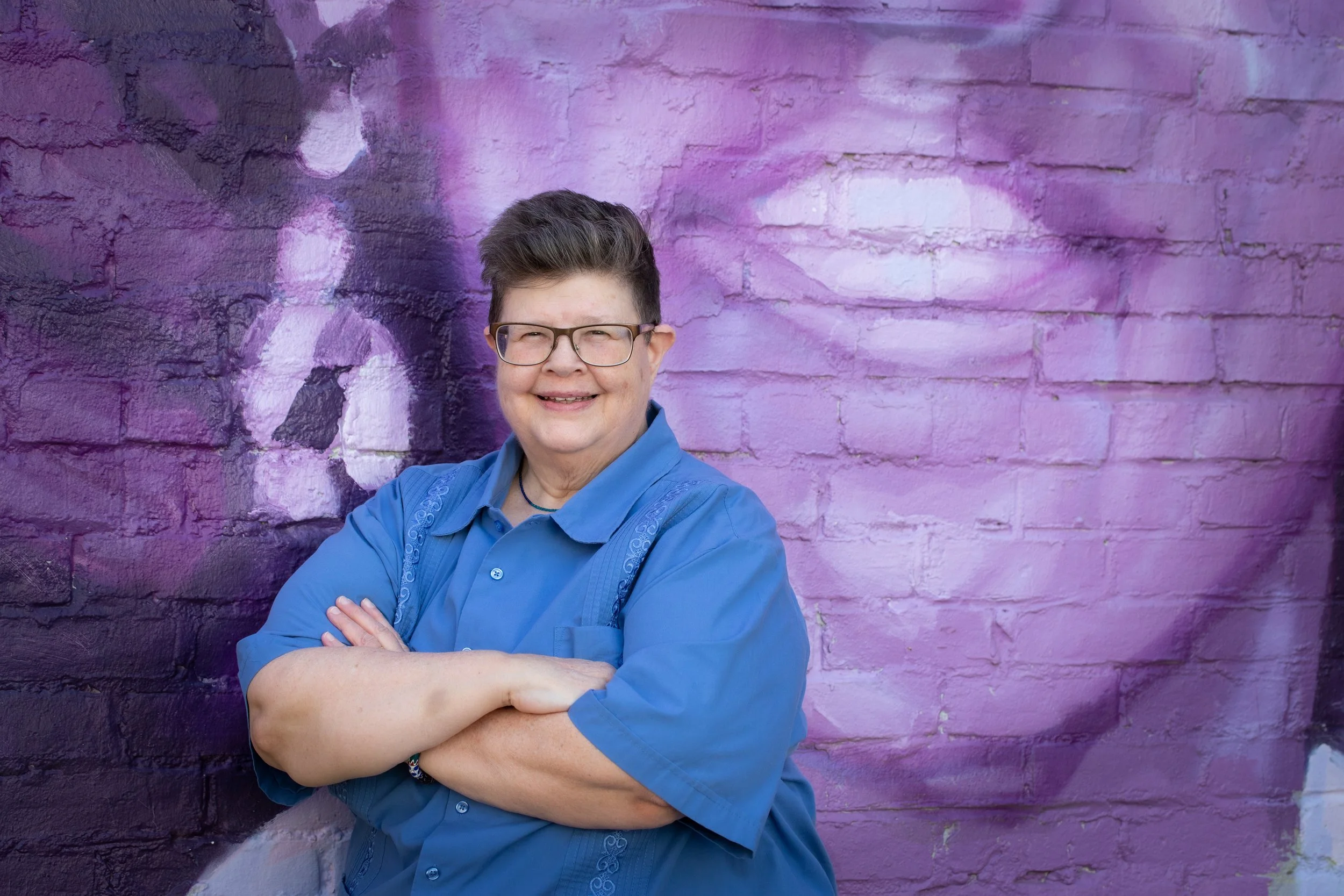 Kathy in a blue shirt standing in front of a mural.