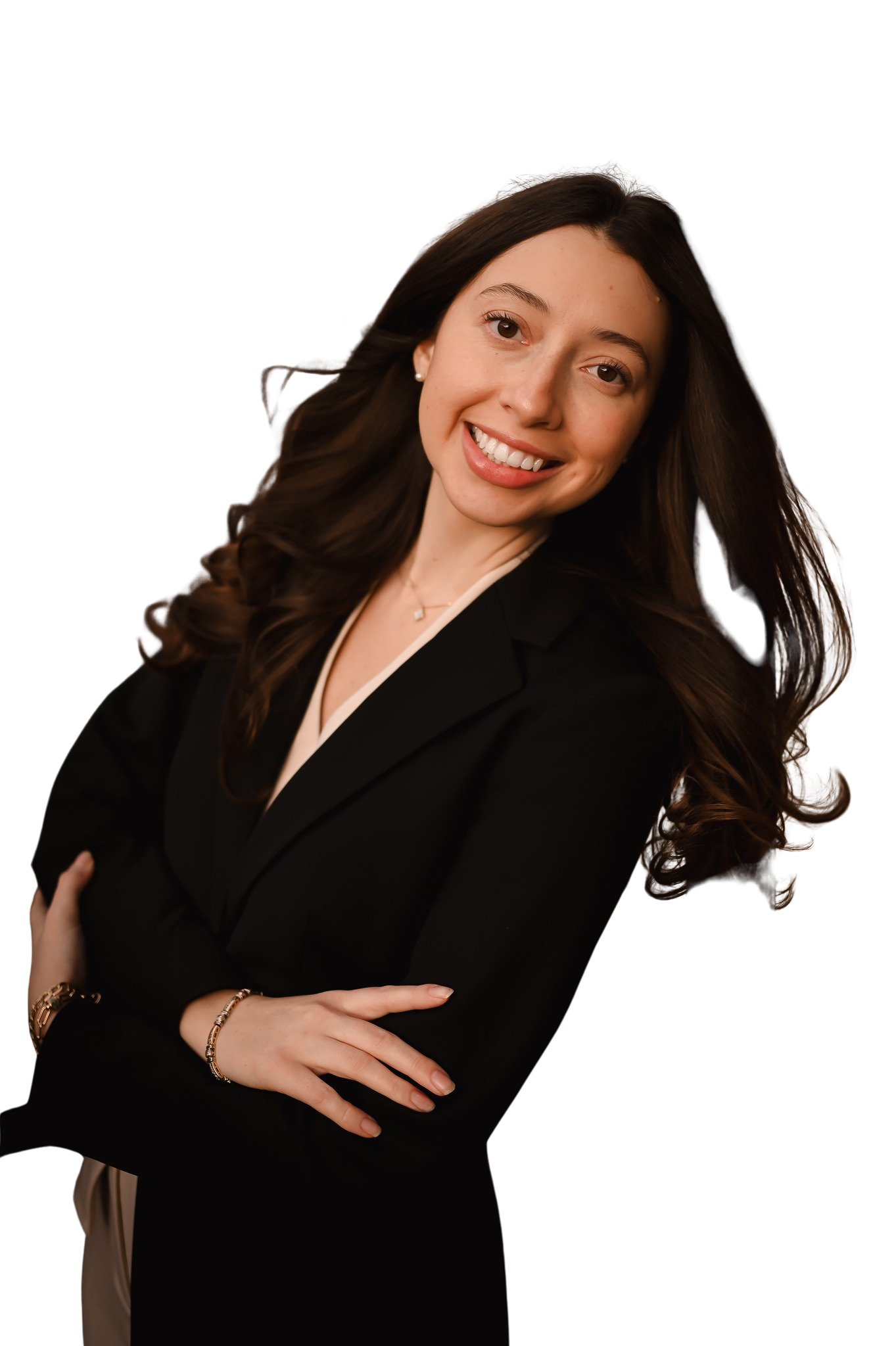 A woman with long brown hair, smiling, wearing a black blazer and jewelry, standing with arms crossed.