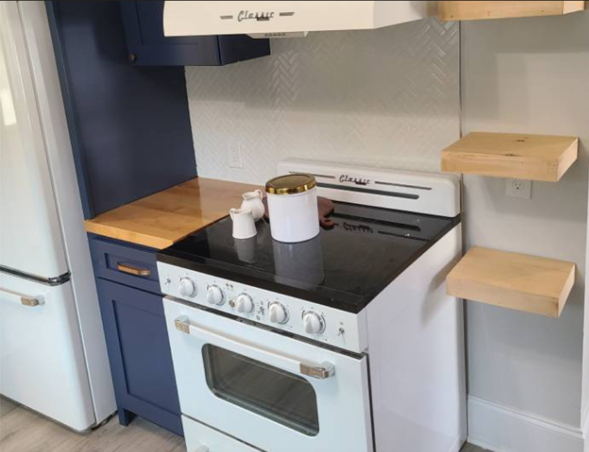Kitchen with blue and white cabinets, a white stove with a black cooktop, and two floating wooden shelves on the wall.