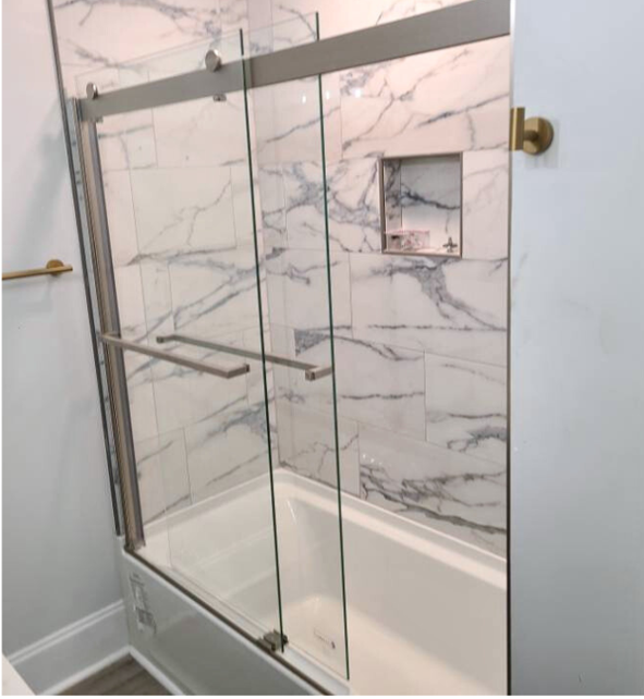 Bathroom with glass shower enclosure, marble wall tiles, built-in shampoo niche, and gold towel bar.