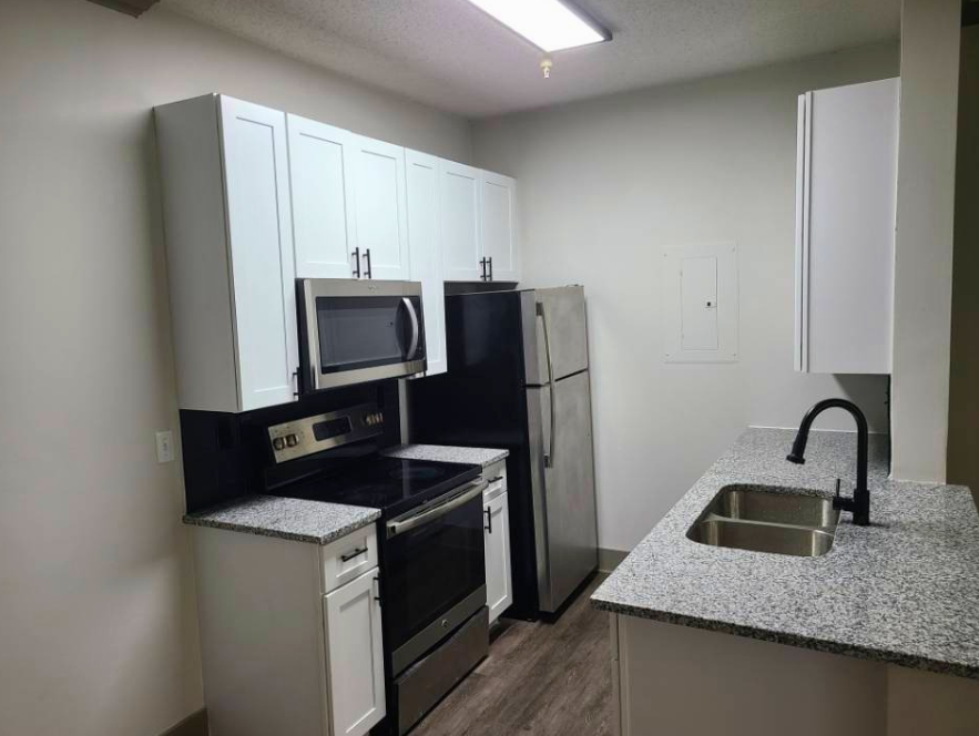 Modern kitchen with white cabinets, stainless steel refrigerator, black stove, microwave, granite countertops, and a double sink with a black faucet.