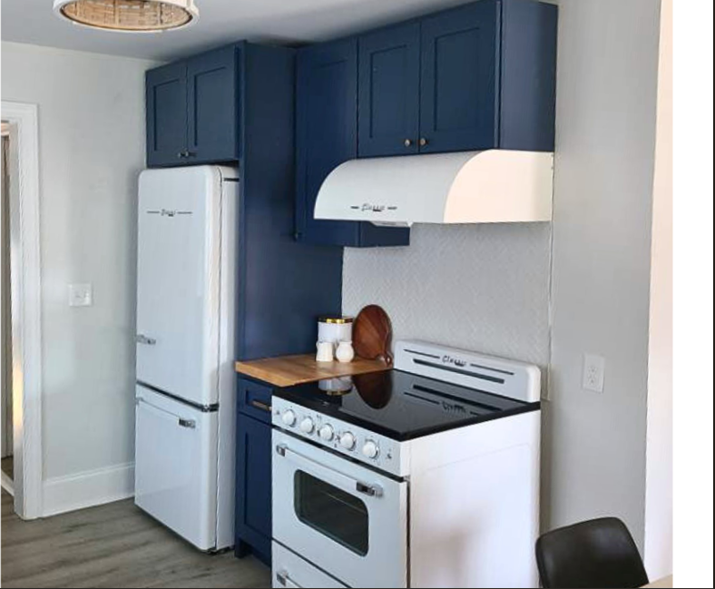 Kitchen with blue cabinets, white refrigerator, white stove, wooden countertop, and a black chair.