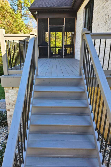 Wooden stairs leading up to a screened-in porch attached to a brick house with black framing, surrounded by trees.