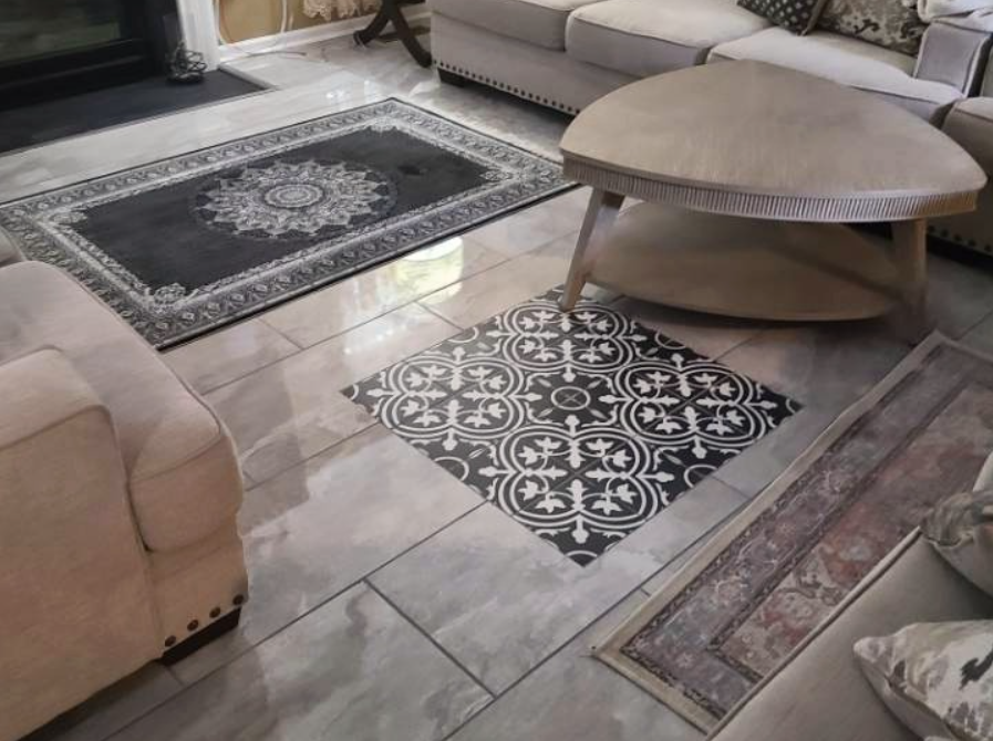 Living room with tiled floor, beige sofas, and multiple patterned rugs, including a black and white patterned tile and a darker decorative rug.