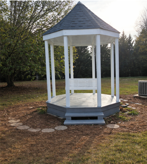 White wooden gazebo with a shingled pointed roof in a grassy backyard.