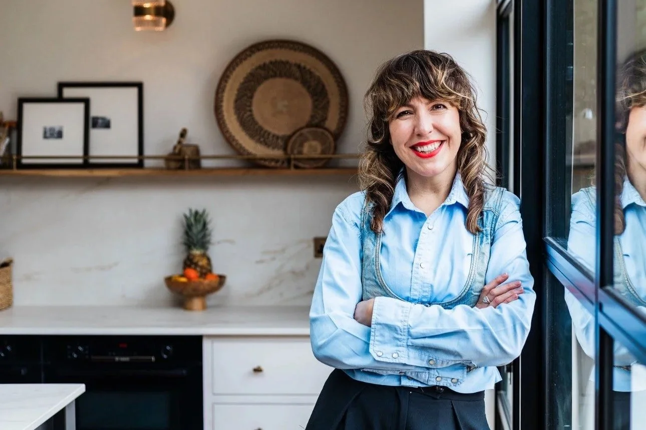 Becs Pearson copywriter smiling with arms crossed leaning against a glass door in a kitchen