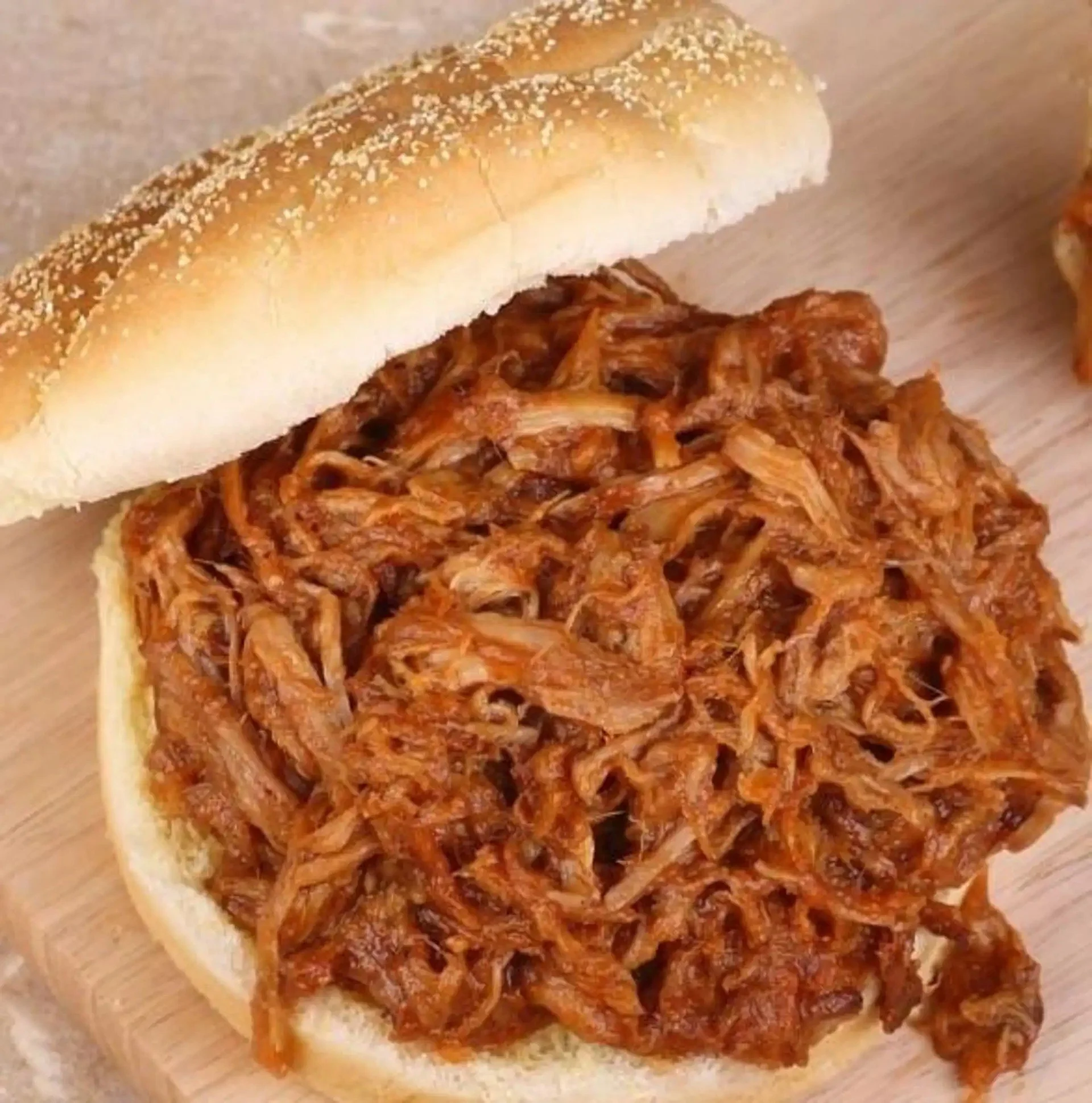A sandwich bun filled with shredded pulled pork barbecue on a wooden surface.