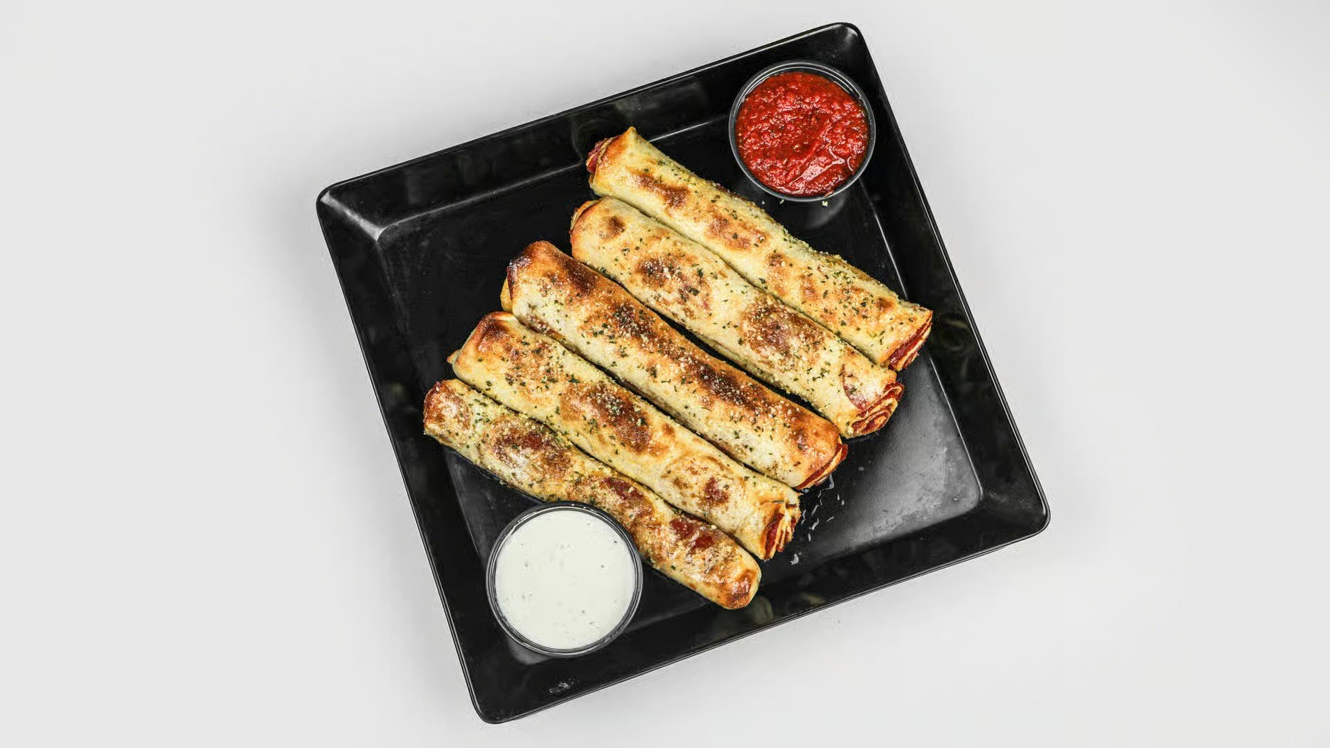 Four cheese-filled jalapeño poppers on a black tray with sides of ranch and salsa