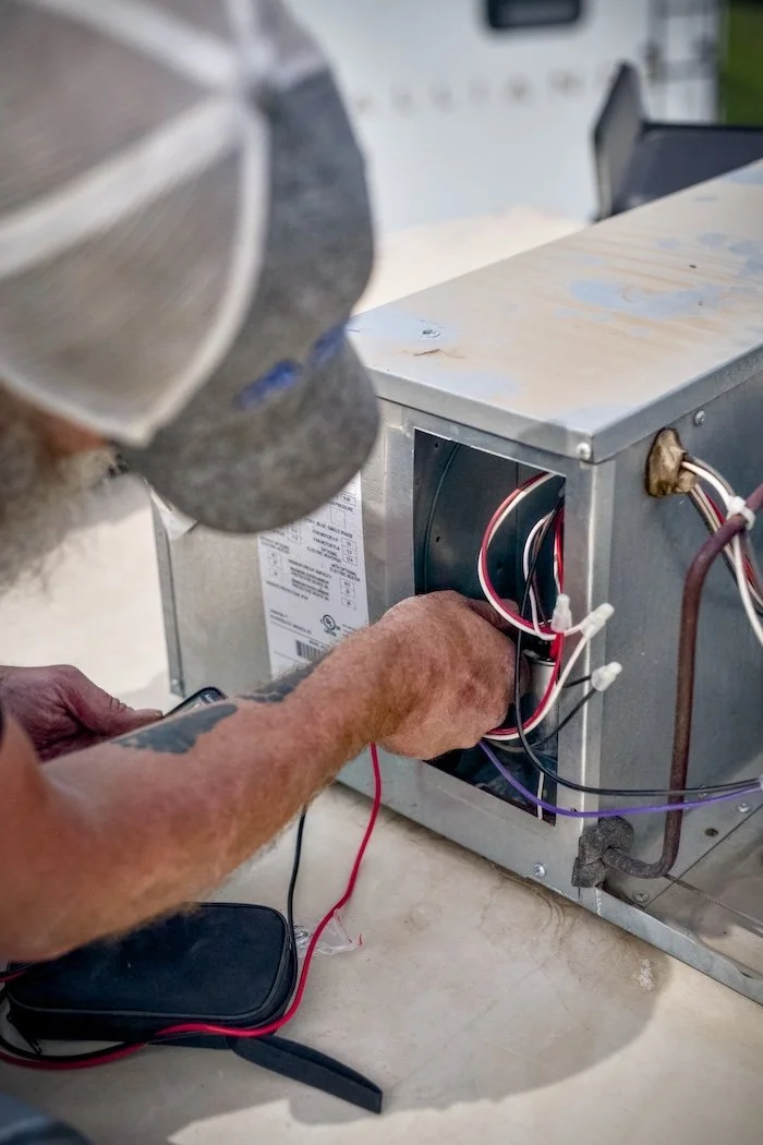 A technician working on a small electrical box with visible wires, outdoors on a table.
