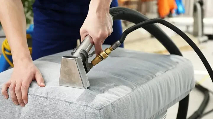 Person cleaning or repairing a gray upholstered cushion or furniture using a handheld cleaning device