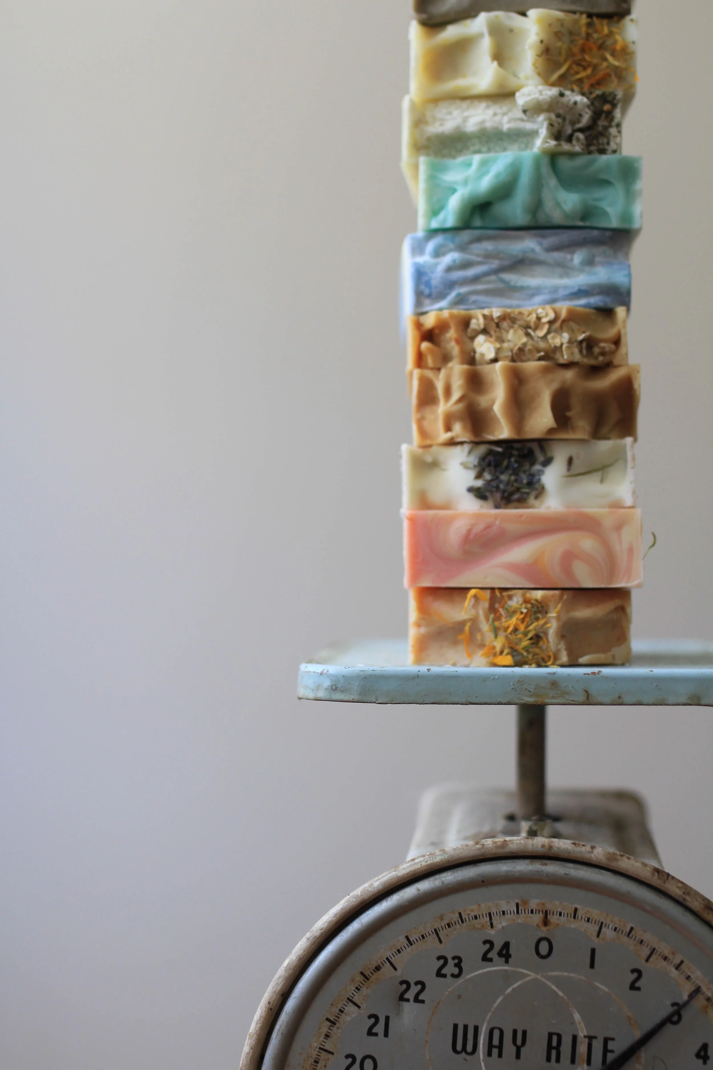 Stack of colorful handmade soap bars on a vintage scale with a white background.