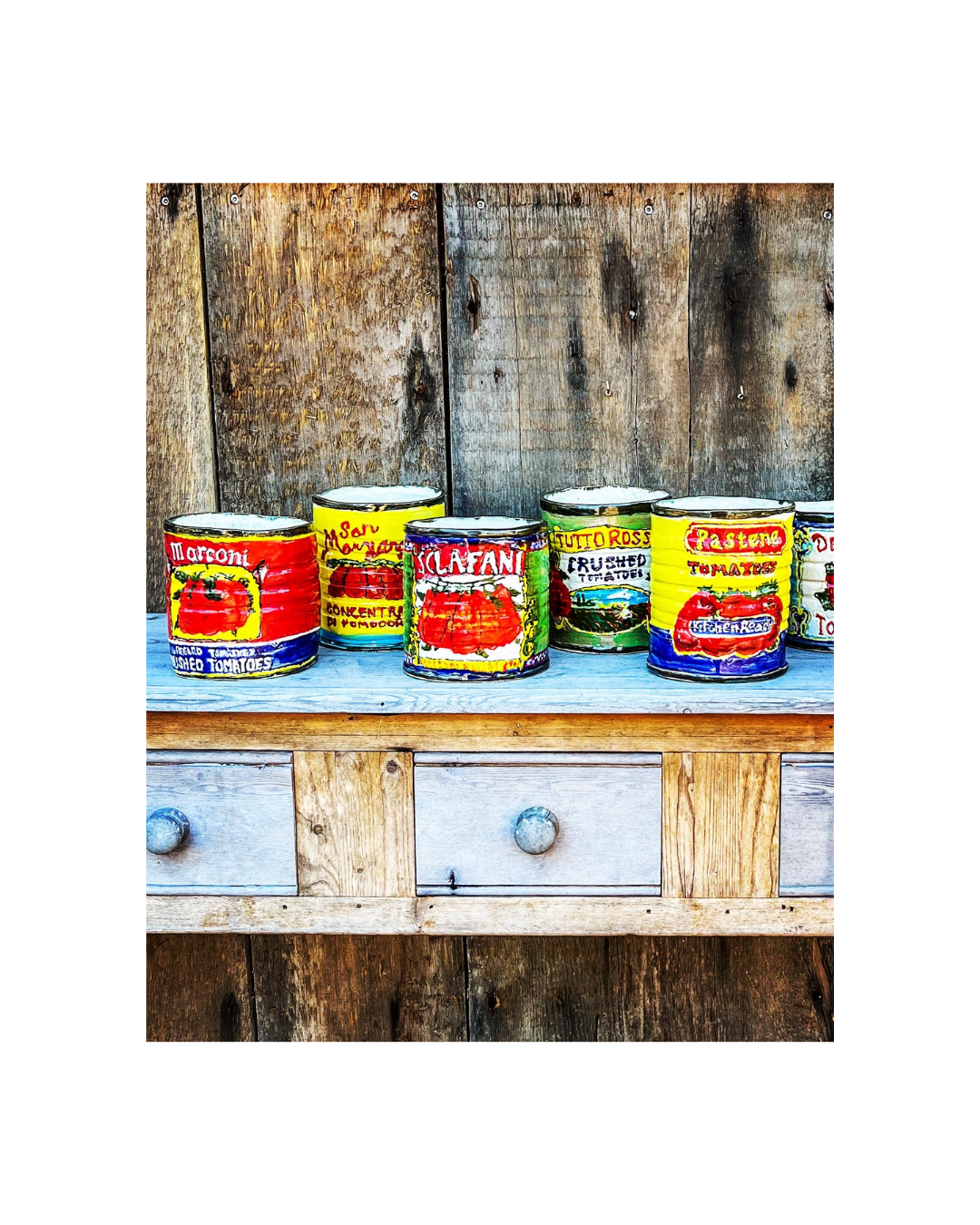 Colorful cans of canned tomatoes lined up on a wooden table against a rustic wooden background.