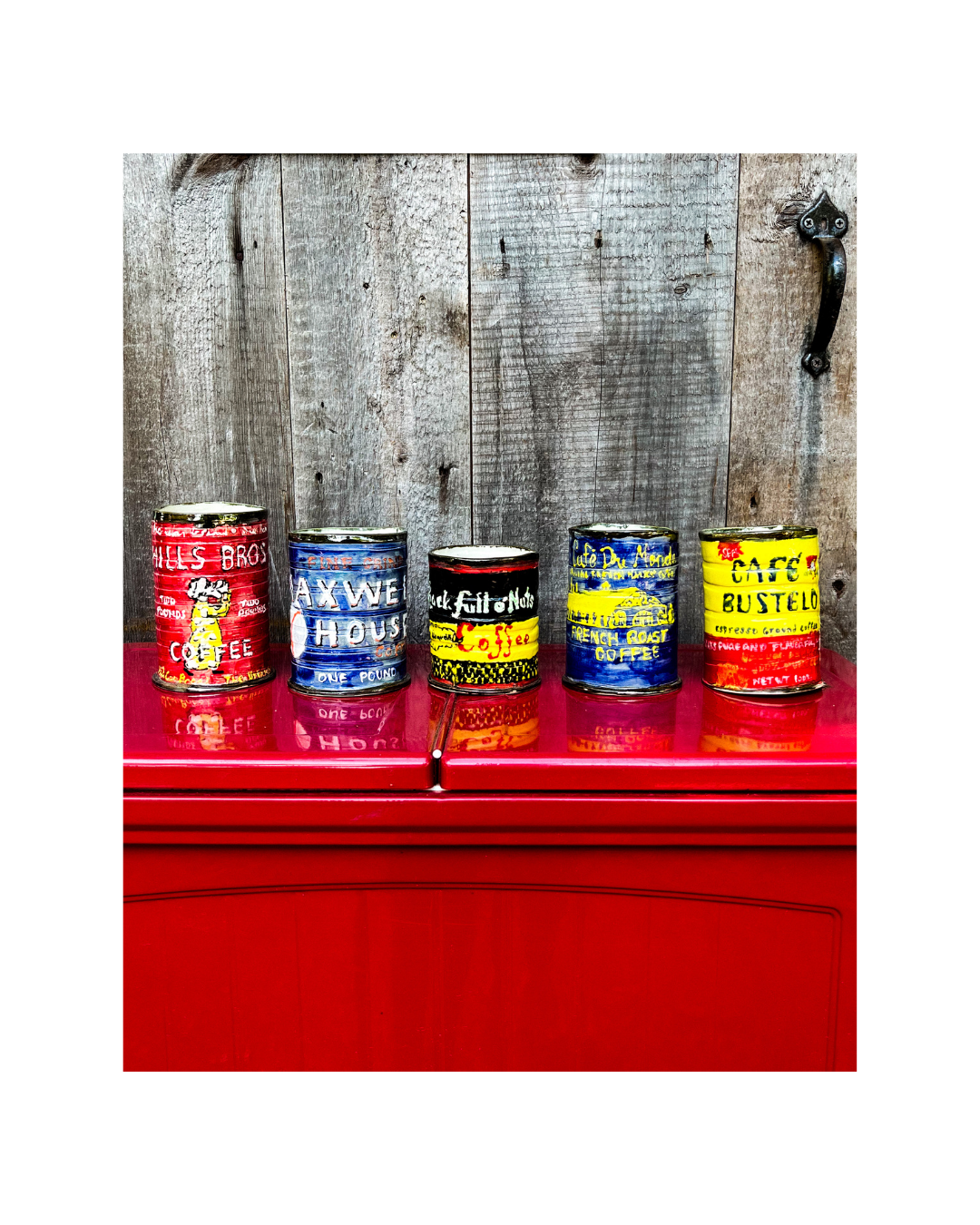 Five vintage inspired ceramic coffee cans with colorful labels on a red surface against a wooden backdrop.