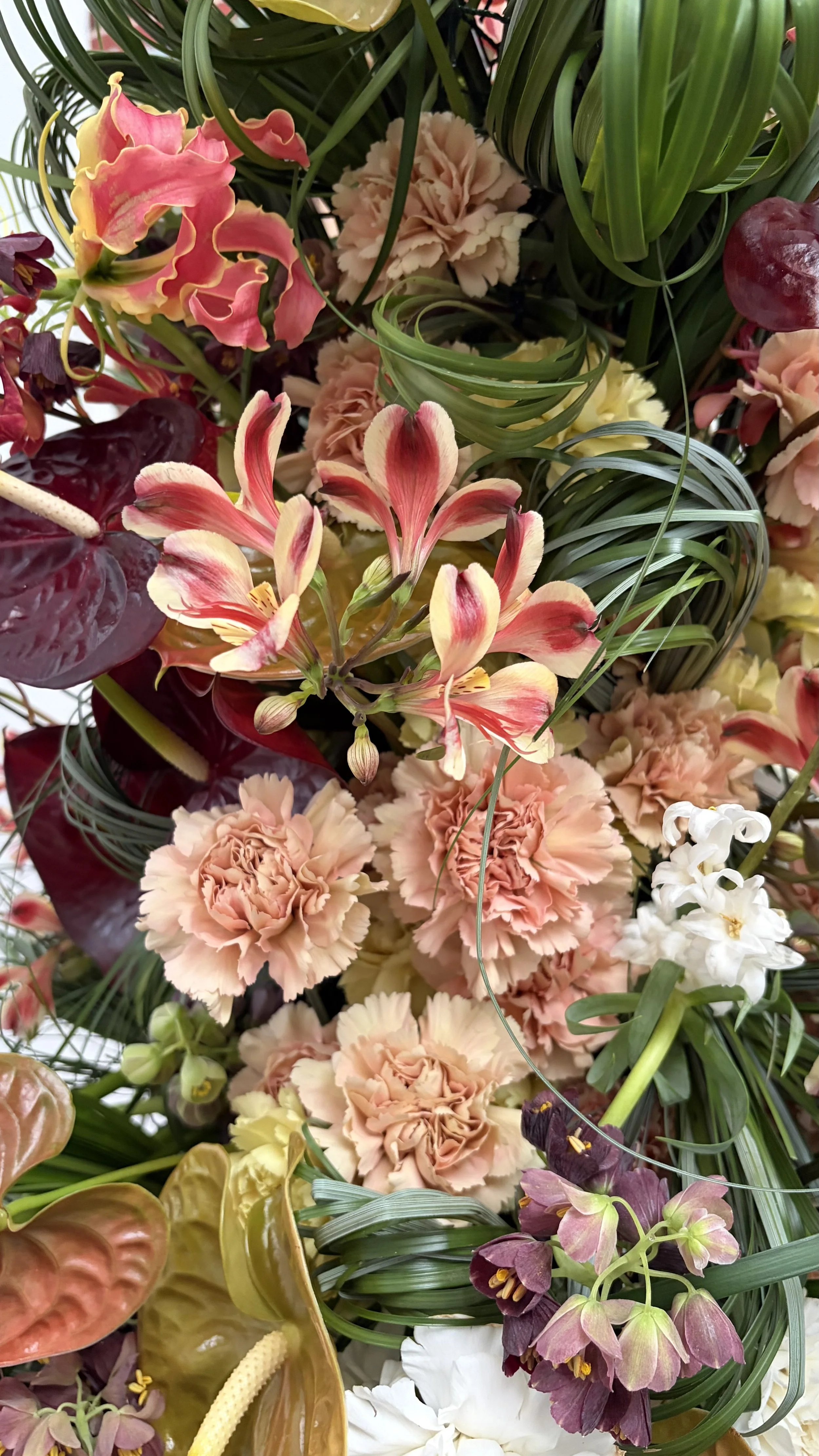 A colorful arrangement of various flowers including pink carnations, white flowers, pink and yellow lilies, and other mixed blossoms with green leaves and grasses.