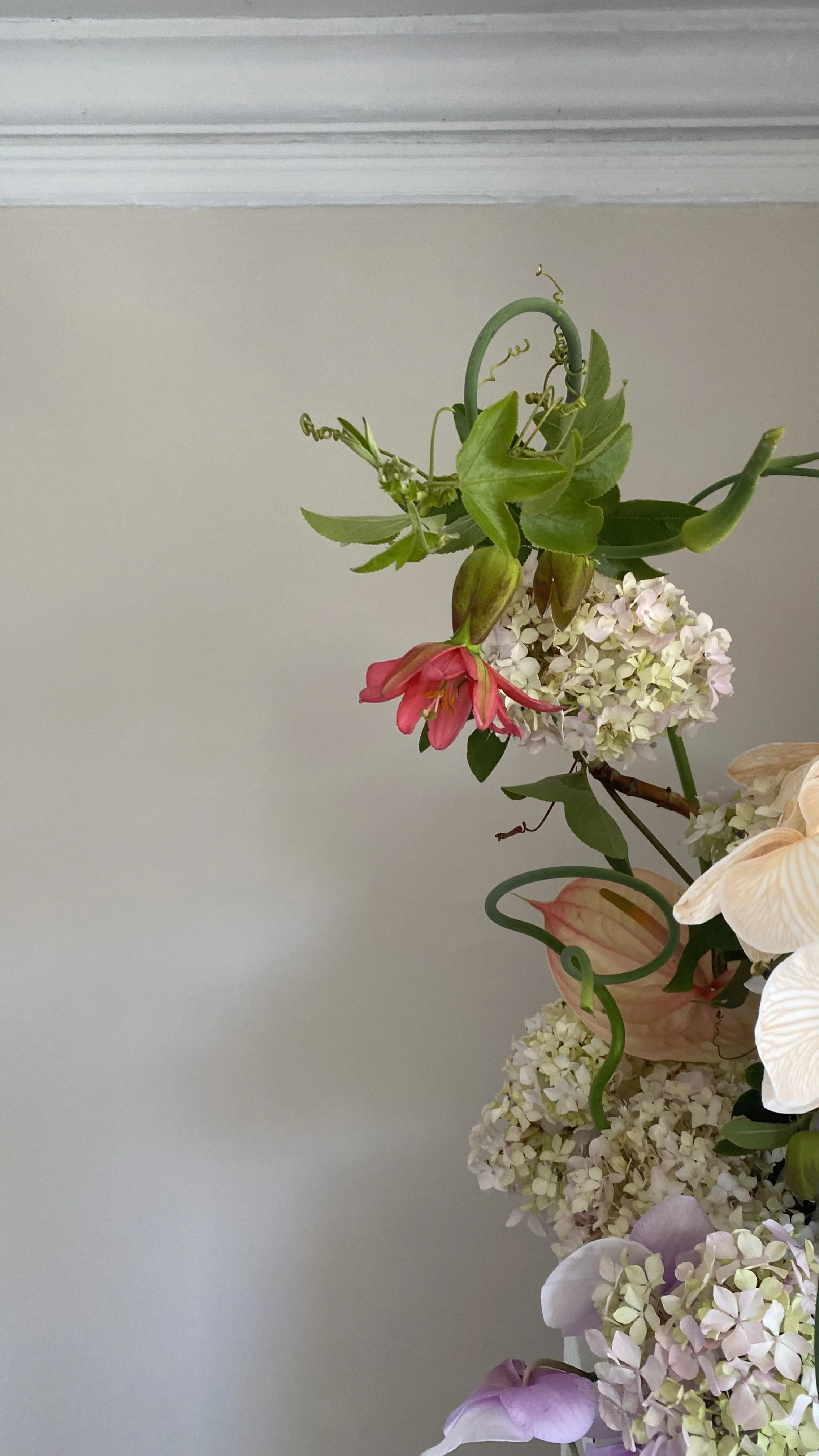 Close-up of a mixed floral arrangement with pink, white, and purple flowers against a plain wall.