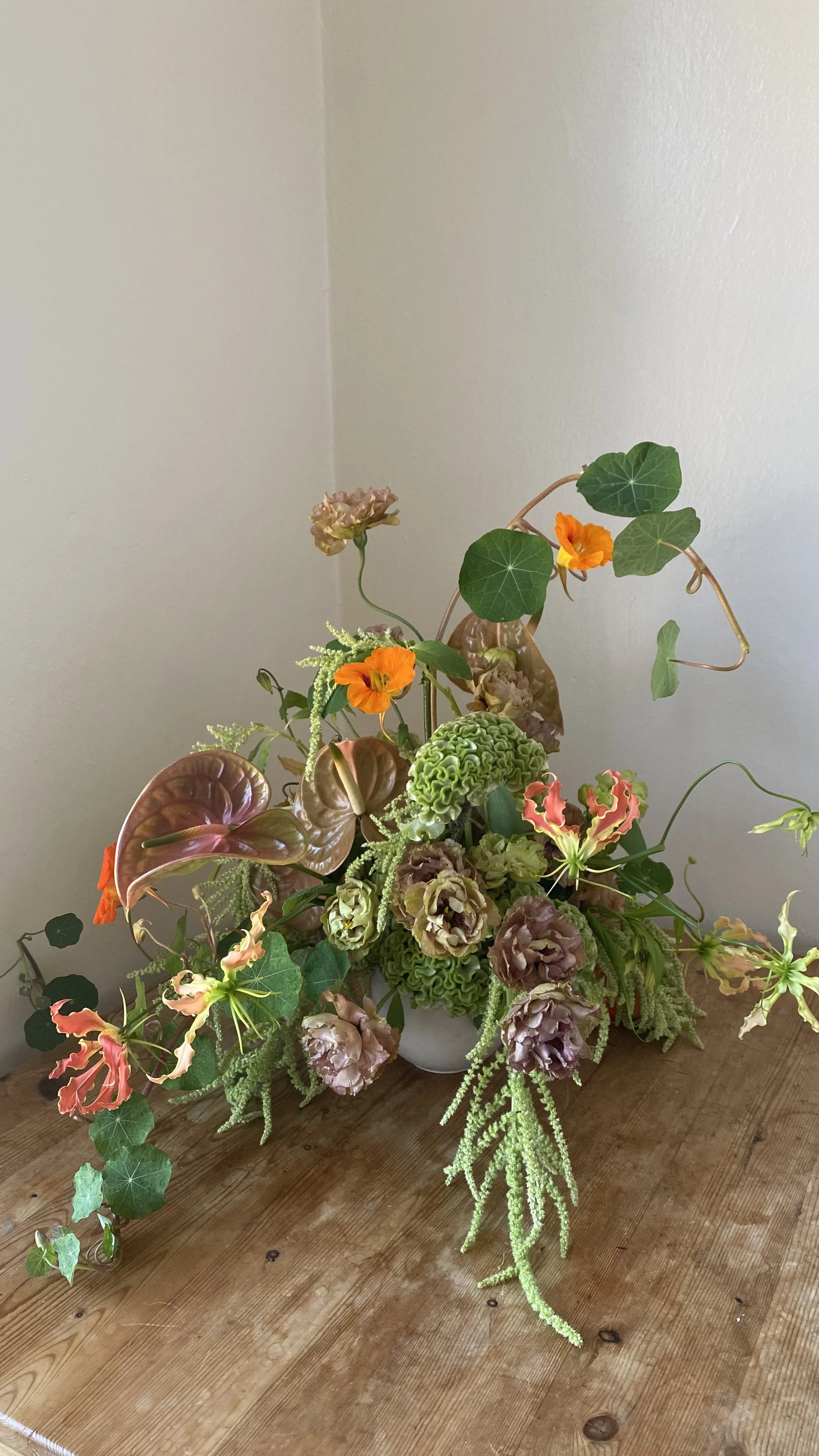 A floral arrangement with various green and pink flowers and leaves on a wooden table against a light-colored wall.