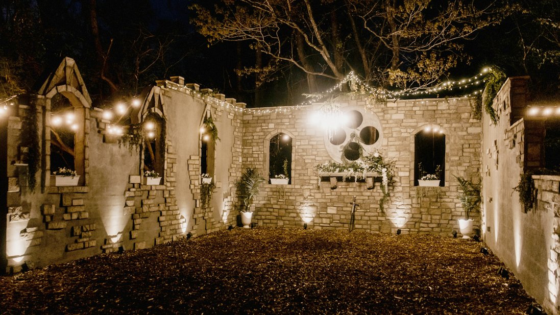 A decorated outdoor patio at night with string lights, potted plants, and a wall featuring a large skull-shaped decoration with circular cutouts.