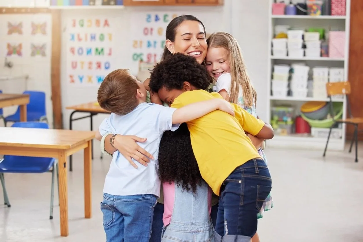 A school contract speech therapist in Wisconsin hugging four children in a classroom, smiling and showing affection.