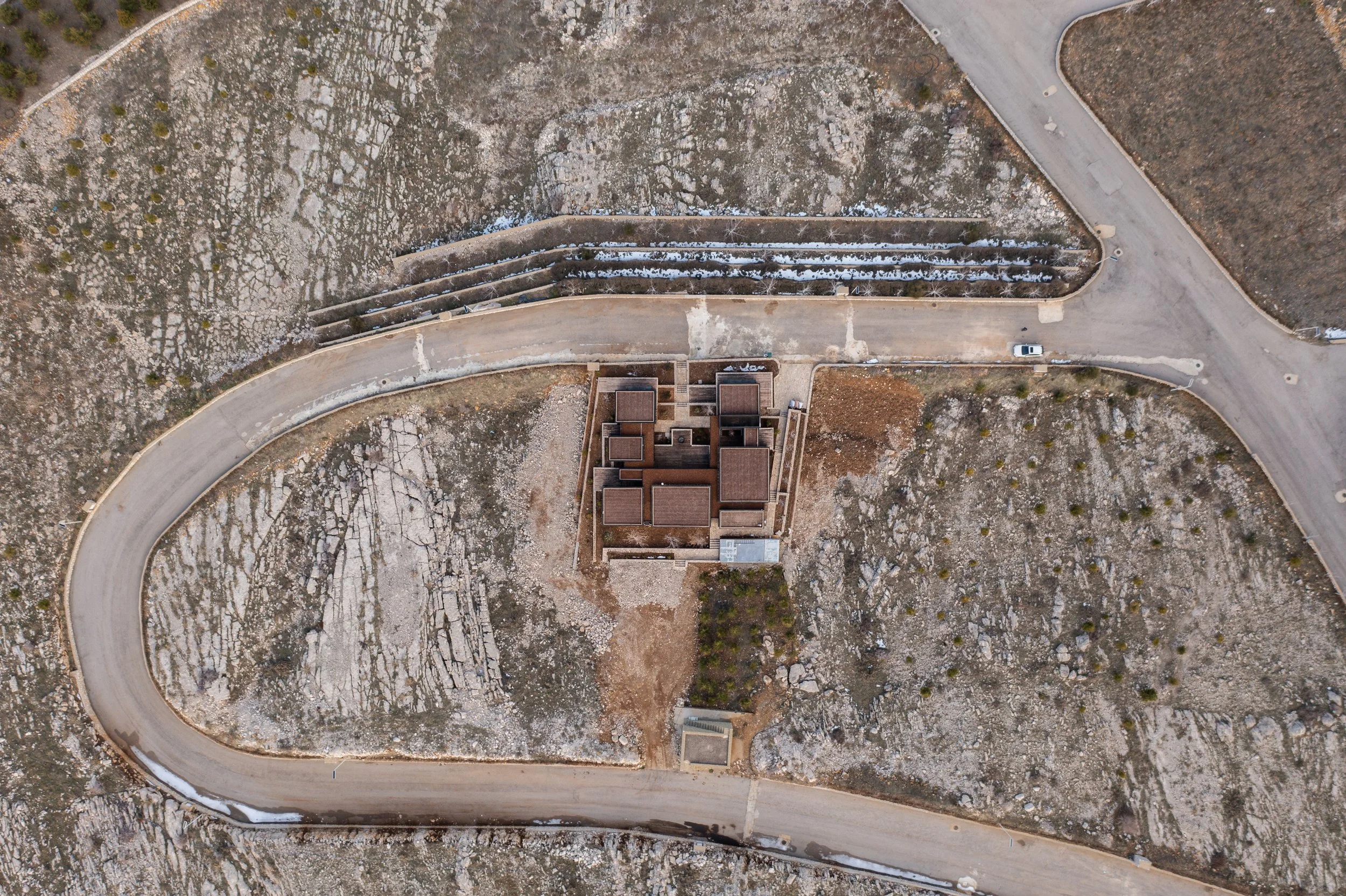 An aerial view of a winding road passing through a rocky, barren landscape with sparse vegetation and a few buildings.
