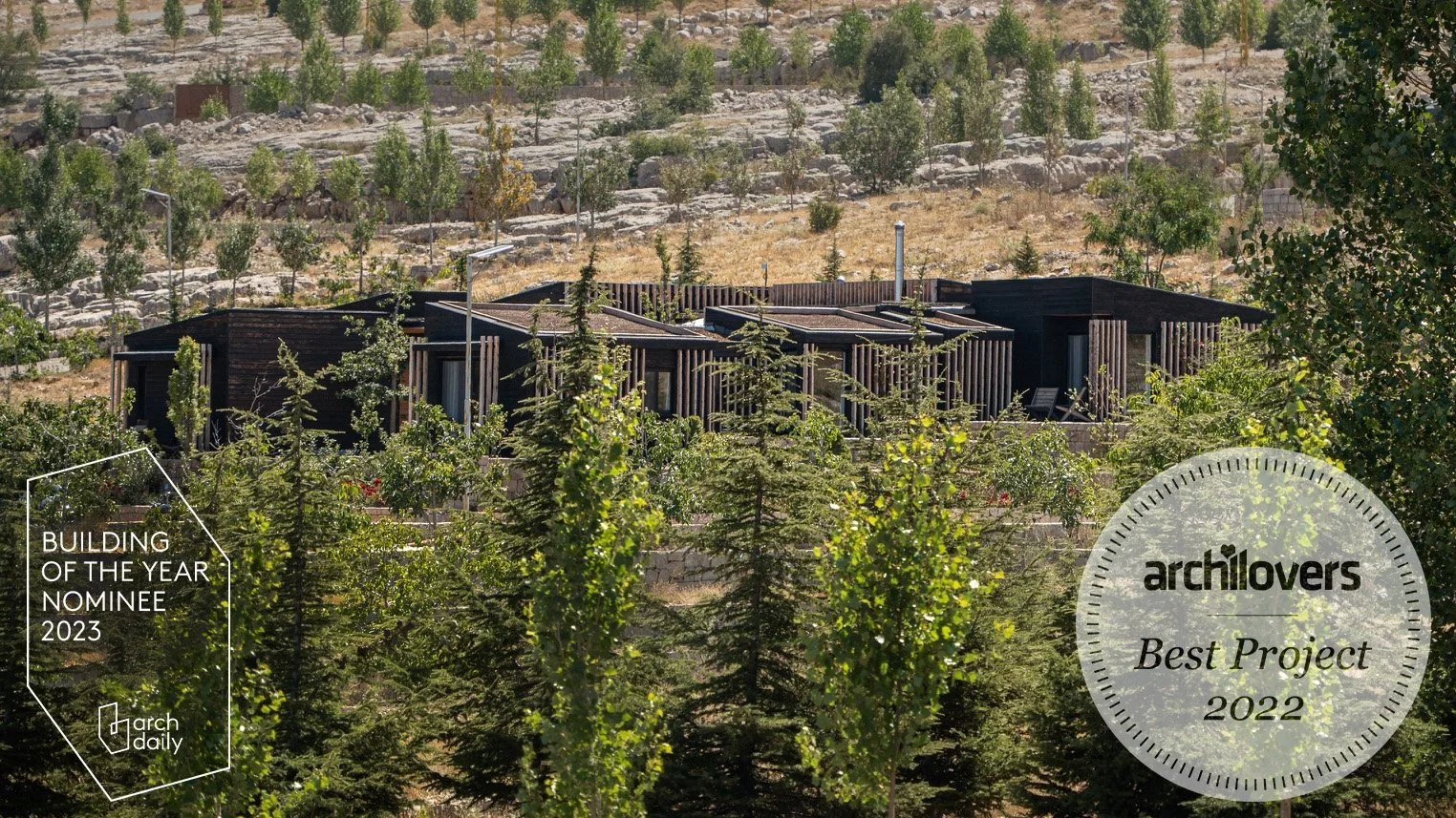 Modern black wooden house surrounded by trees, with a hillside in the background, awarded 'Best Project 2022' by archilovers and a 'Building of the Year Nominee 2023' by arch daily.
