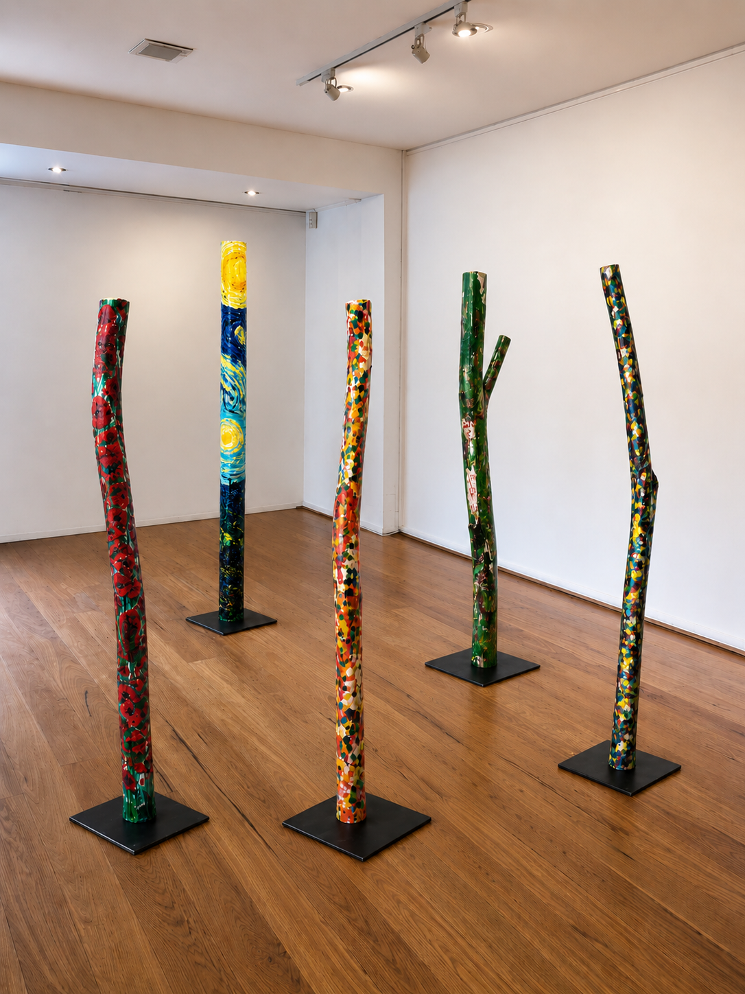 Fünf Skulpturen, die wie bunte, bemalte Baumstämme aussehen, sind in einer Galerie aufgestellt.
