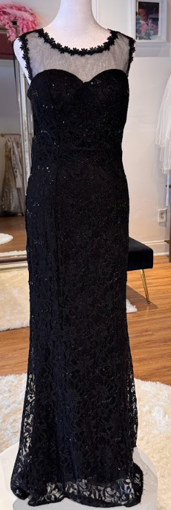 Black evening gown with lace overlay and sheer neckline on a mannequin in a room.
