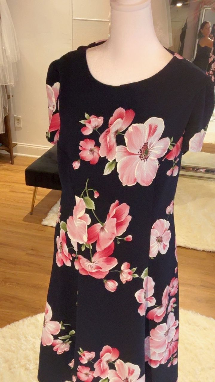 A black dress with pink and white floral pattern displayed on a mannequin.