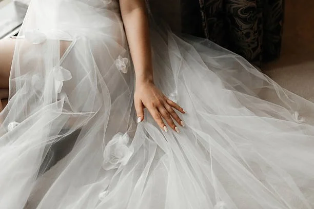 Close-up of a bride's hand resting on her wedding dress, which is made of tulle with decorative flowers.