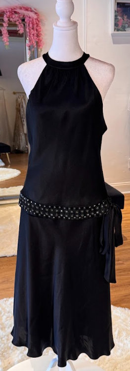 Black sleeveless dress with a high neckline and a bejeweled waist, displayed on a mannequin in a clothing store.