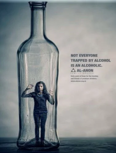 A woman stands inside a large transparent bottle with her hands pressed against the glass. Next to the bottle is a message stating, "Not everyone trapped by alcohol is an alcoholic."