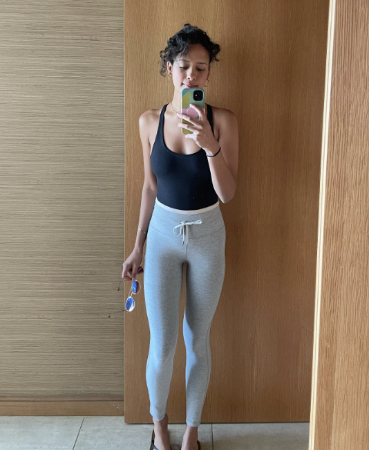 Hannah taking a mirror selfie, wearing a black tank top, light gray sweatpants, and holding sunglasses.