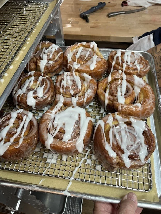 Cinnamon rolls with icing on a wire rack, cooling after baking in a kitchen.