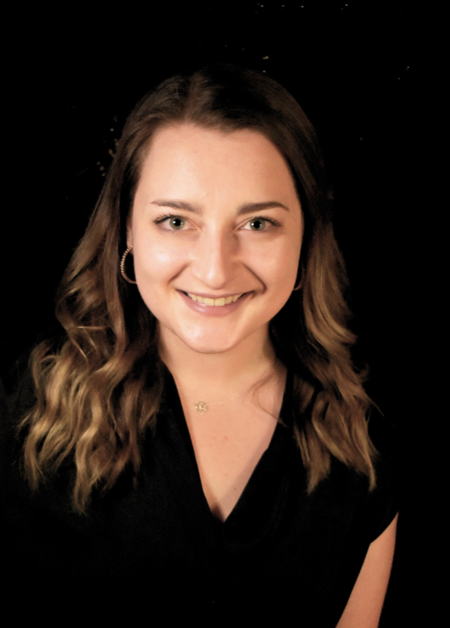 A smiling woman with wavy brown hair, wearing hoop earrings and a black top, against a dark background.
