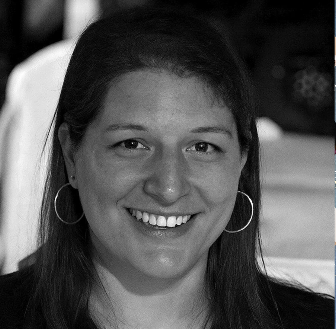 Black and white close-up of a smiling woman with long hair, hoop earrings, and visible teeth.