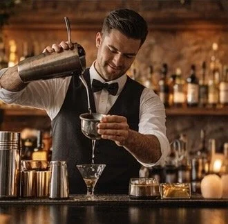 A bartender pouring a cocktail into a glass at a bar.