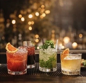 Three colorful cocktails on a bar counter with blurred festive lights in the background.