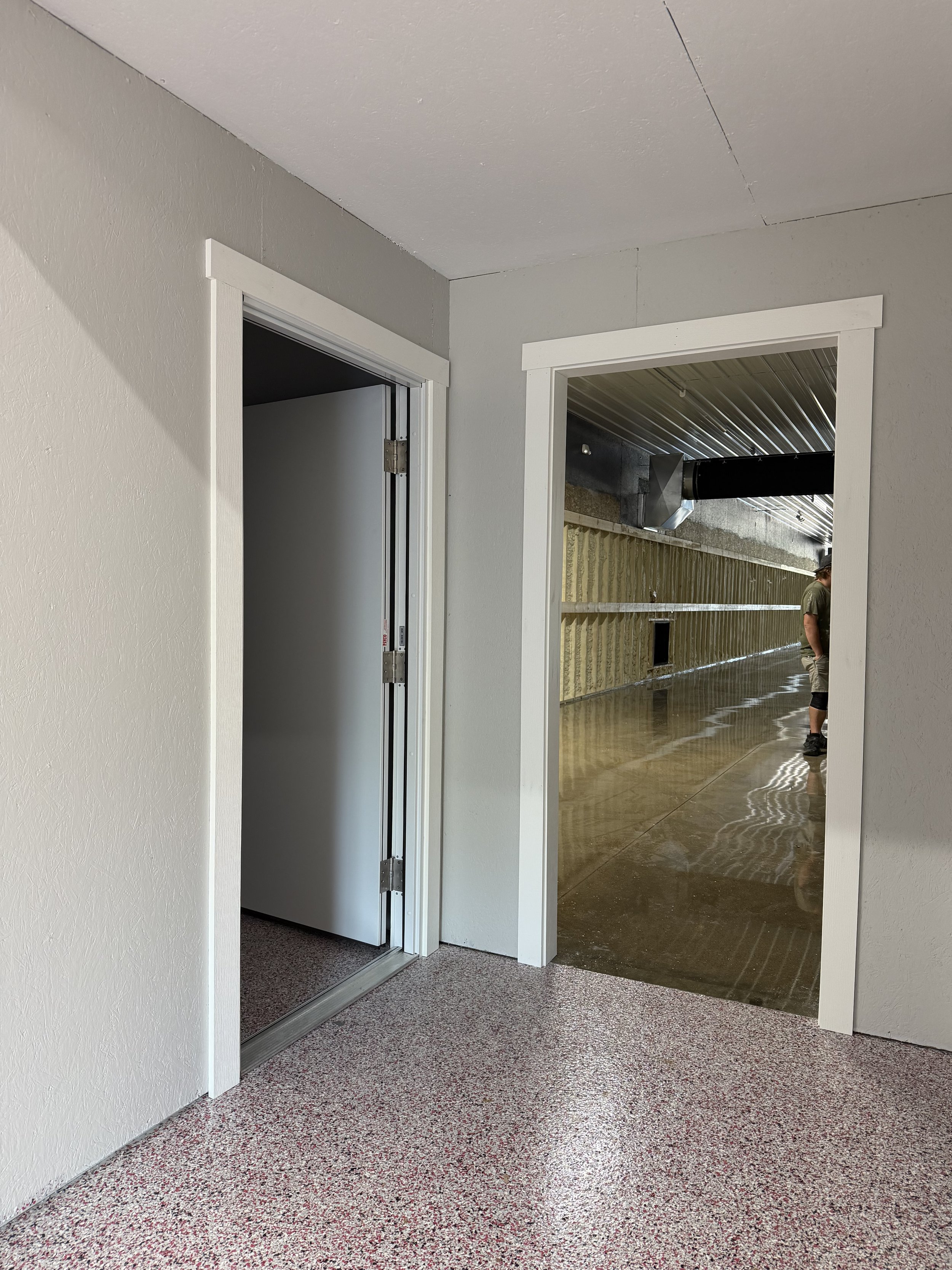 Indoor hallway with sliding glass door on the left, open doorway on the right revealing a shiny, reflective floor and a partially visible person standing in the distance.