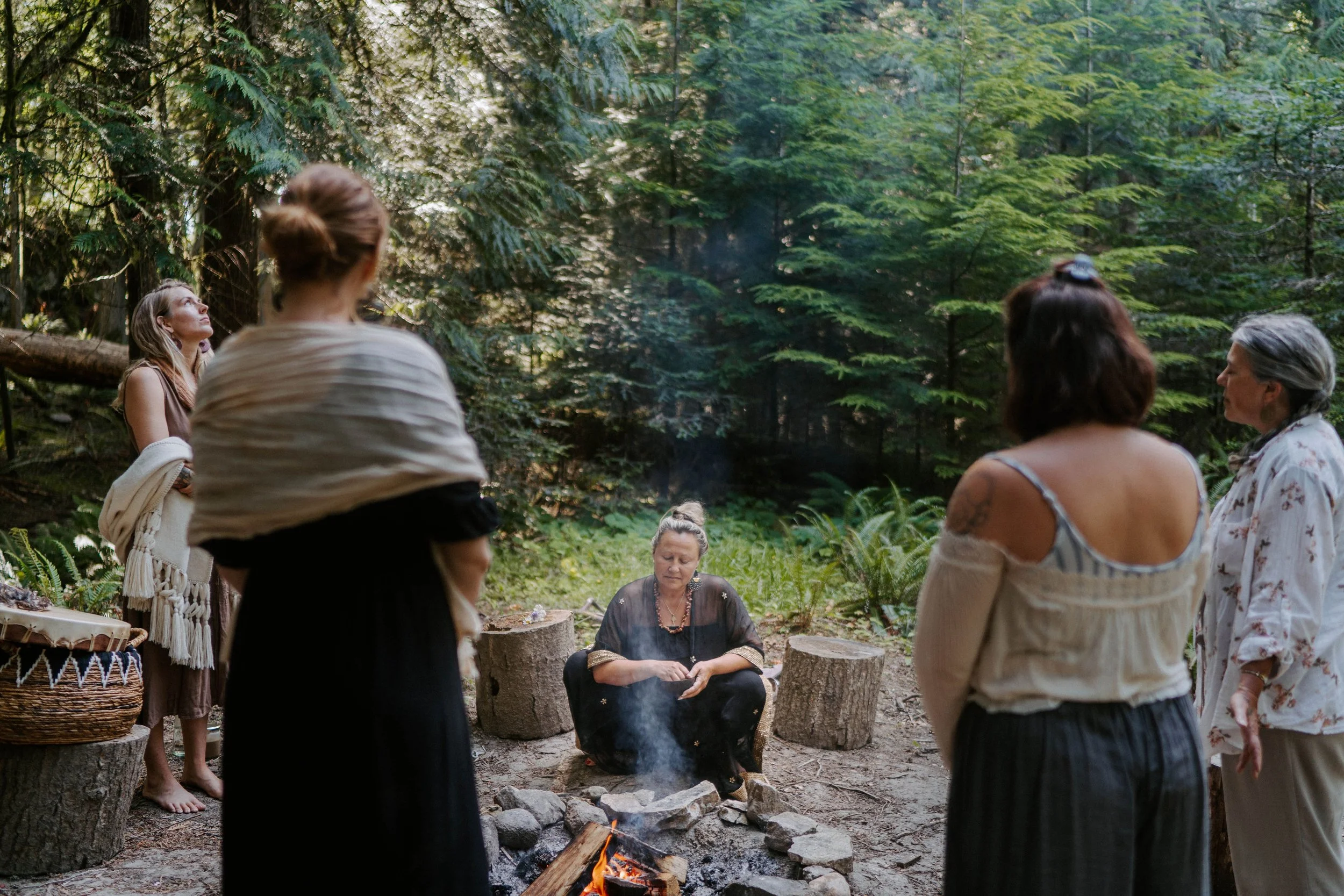 Group of women gathered around a campfire in a forest.