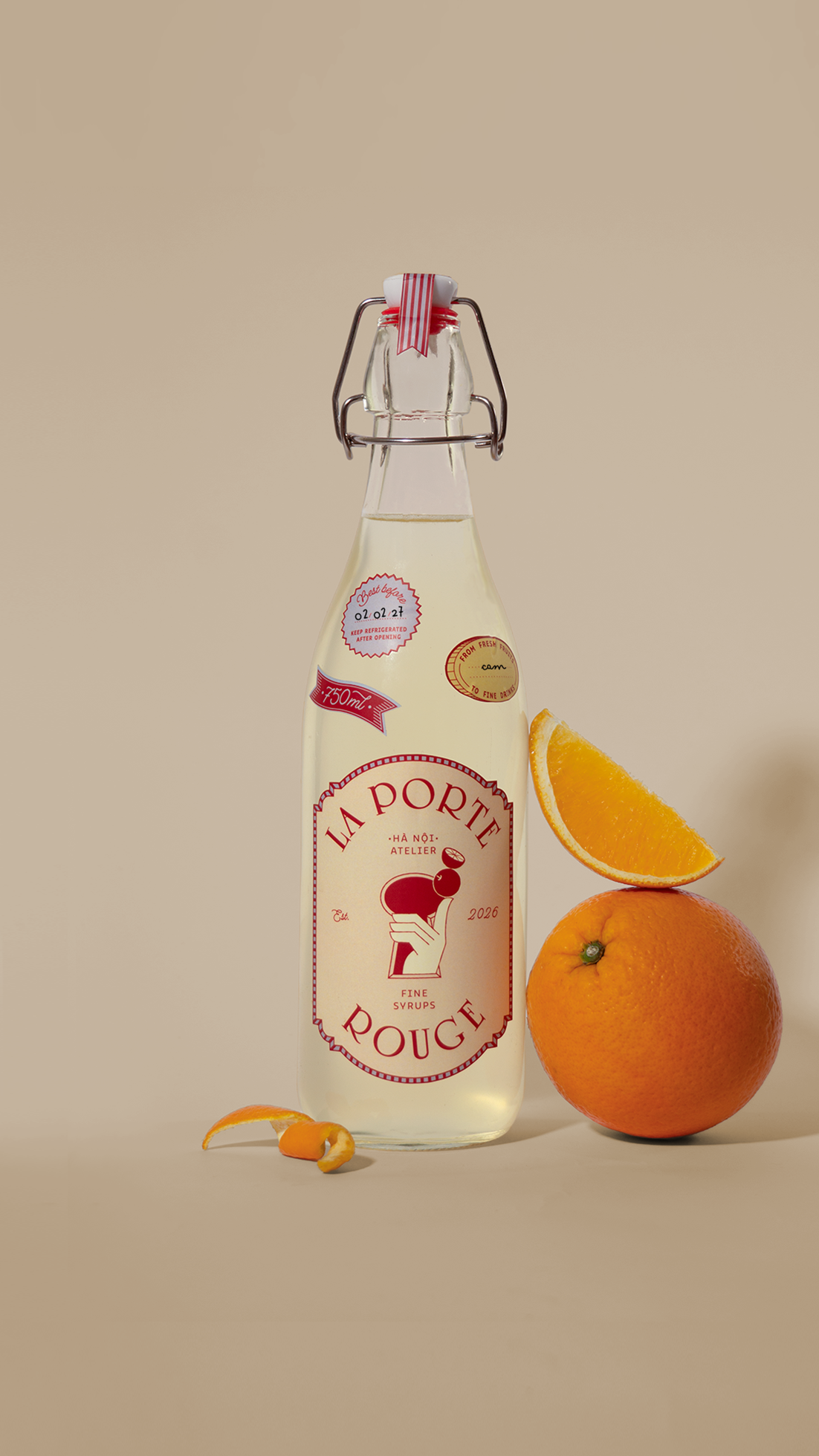A glass bottle of syrup labeled 'La Porte Rouge' with oranges and orange slices beside it on a beige background.