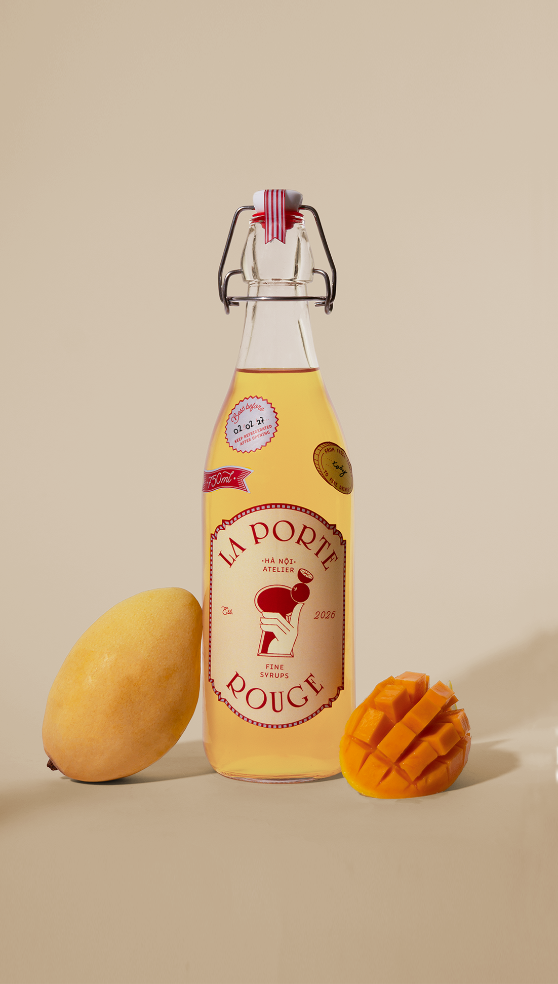 A bottle of La Porte Rouge syrup next to a whole mango and a cubed mango on a beige background.
