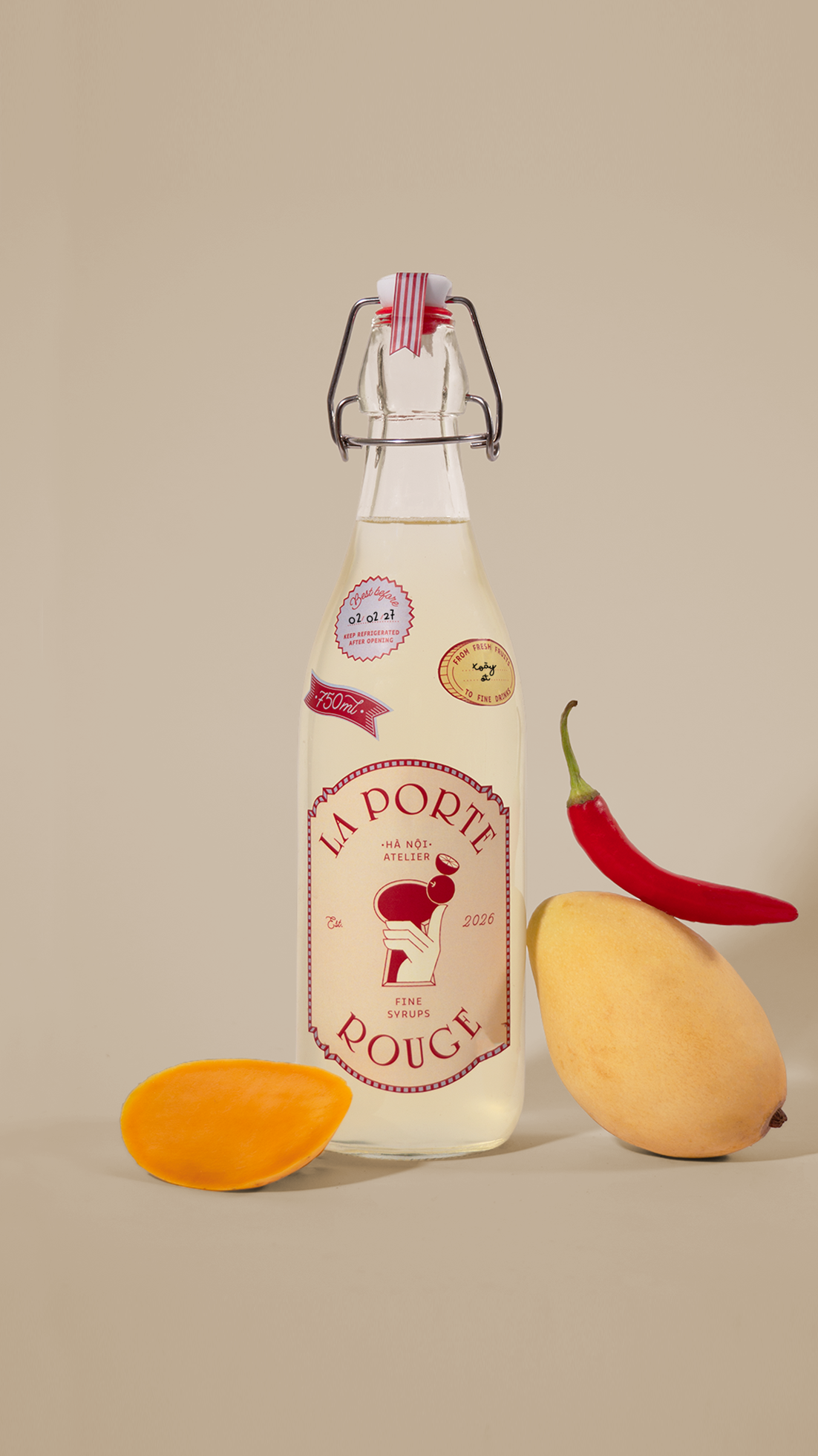 A bottle of La Porte Rouge syrup with a red chili pepper and a pear beside it, and a slice of mango in the foreground.