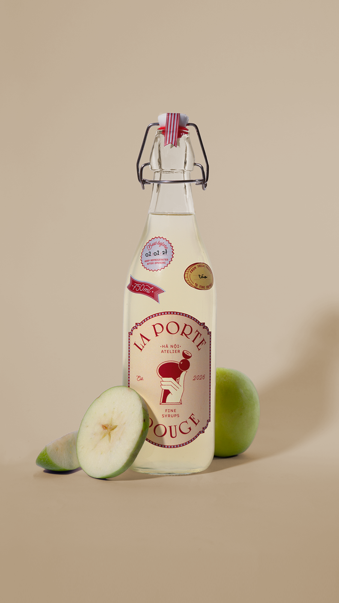 A glass bottle of syrup labeled "La Porte Rouge" with sliced green apples around it on a beige background.