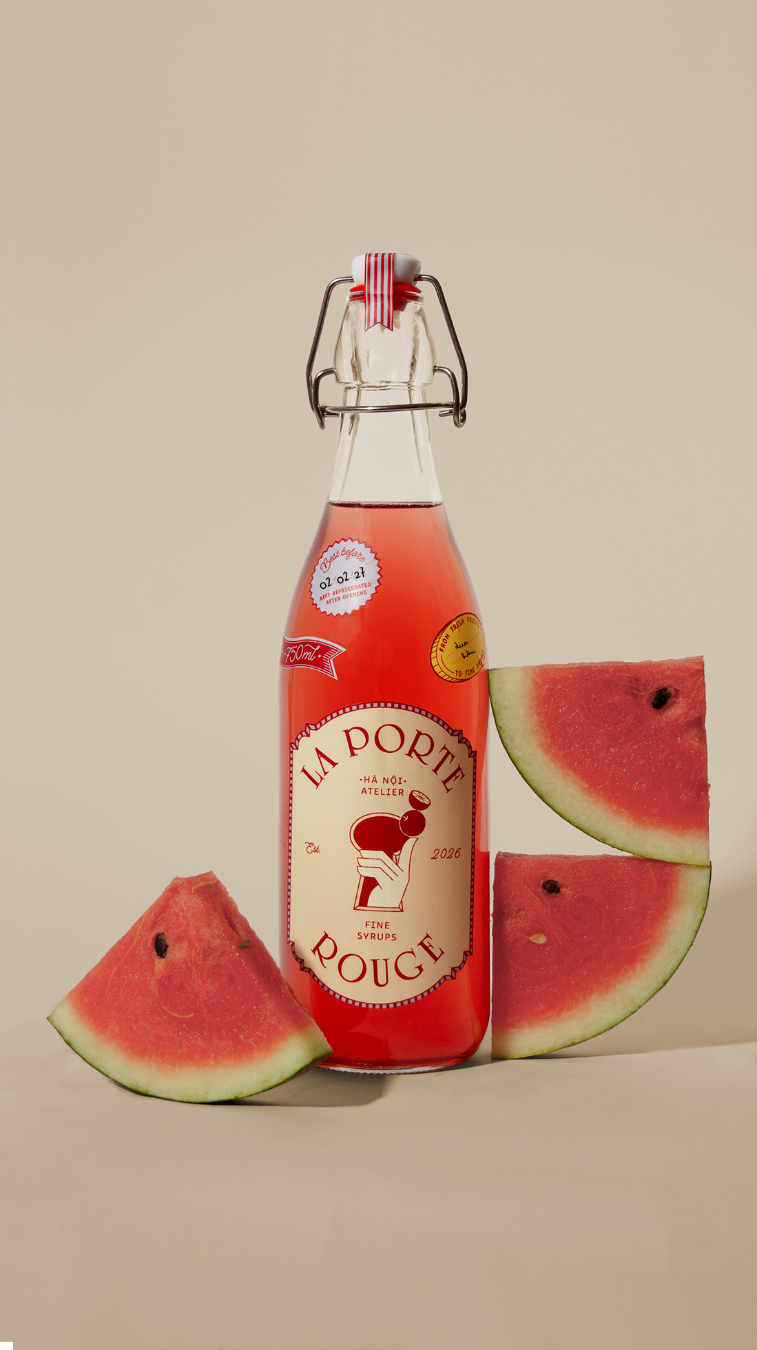 A glass bottle of pink watermelon syrup with a flip-top cap, surrounded by slices of watermelon on a plain background.