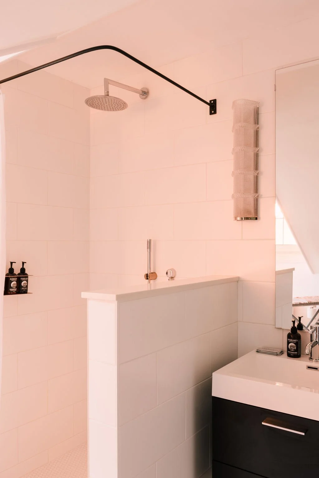 A modern, minimalist bathroom with a shower area and a vanity with a sink, soap dispensers, and towels.