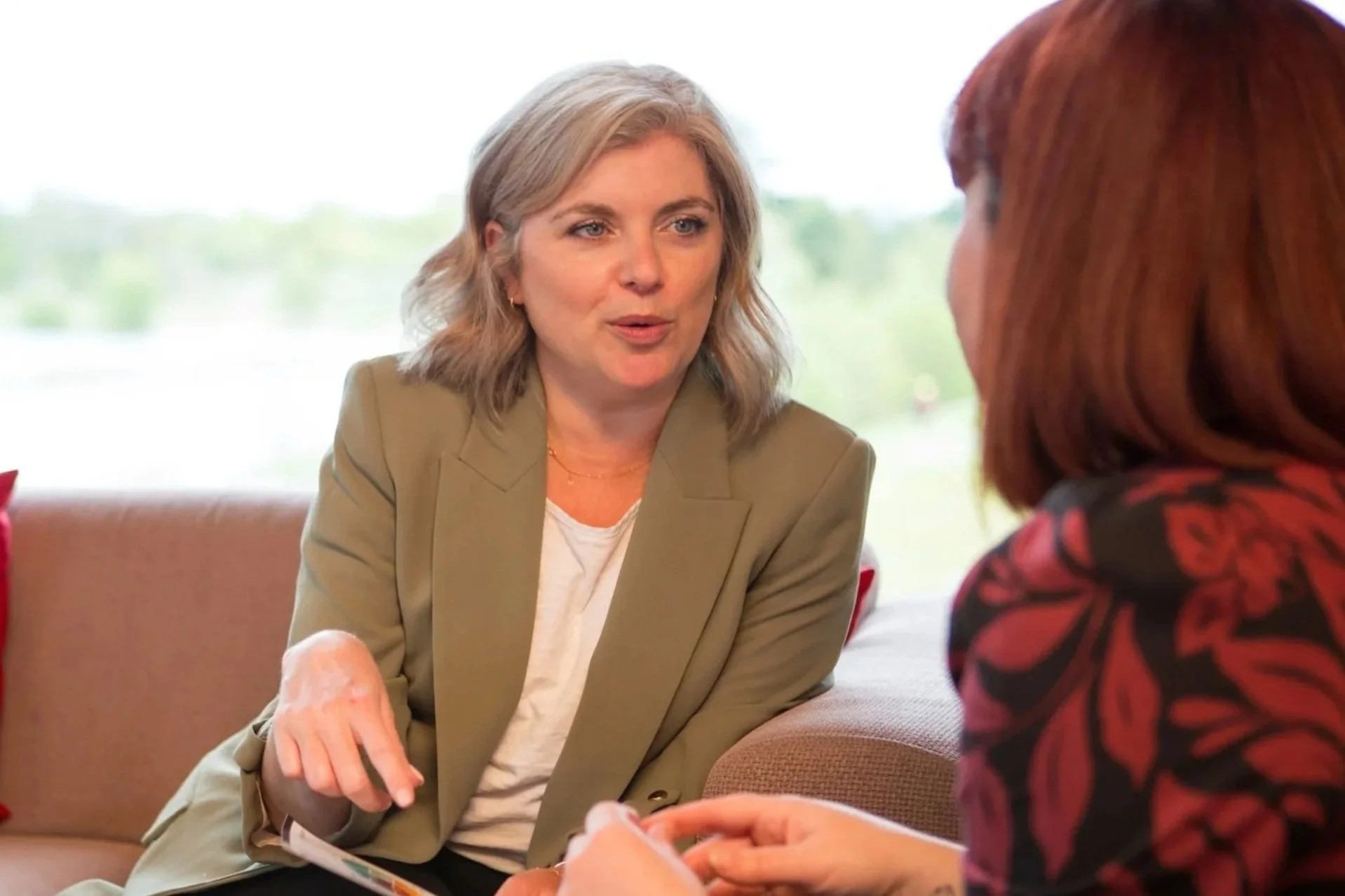 Woman in green smart jacket having a 1-1 coaching session with a woman. The coach is referring to a handout profile report of framework psychometric The GC Index.