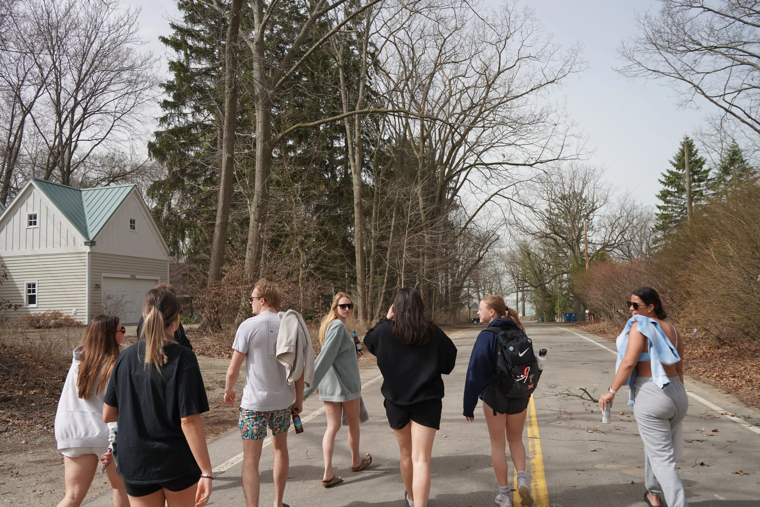 Group of young people walking on a street in a residential neighborhood during daytime, with leafless trees and houses in the background.