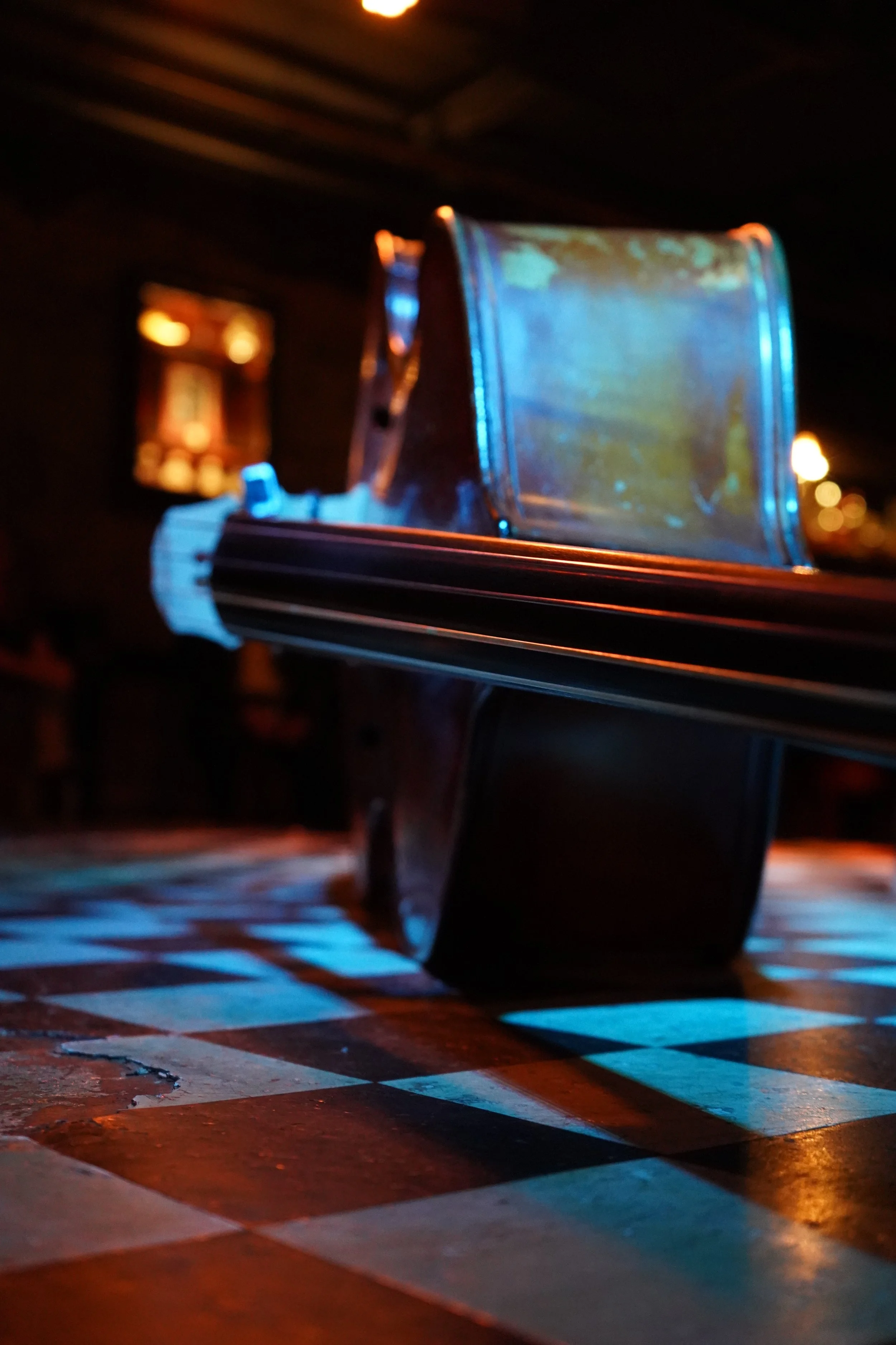 Close-up of a vintage car door with a metallic blue finish, illuminated by warm ambient lighting, with a checkered flooring in the foreground and a blurred interior background.