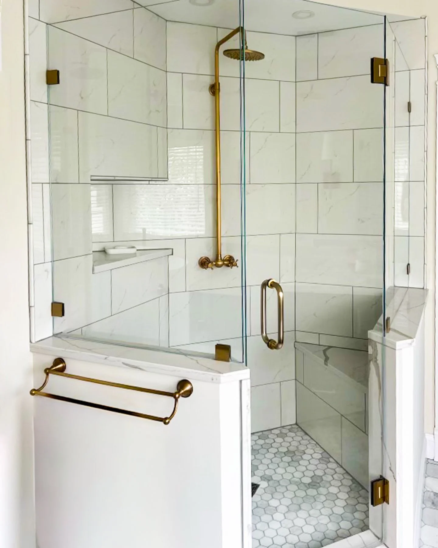 Custom shower with large format marble porcelain tile walls, marble hexagon floor tile, frameless glass enclosure, and brushed gold fixtures — Artisan Tile Creations, Crystal Lake, IL