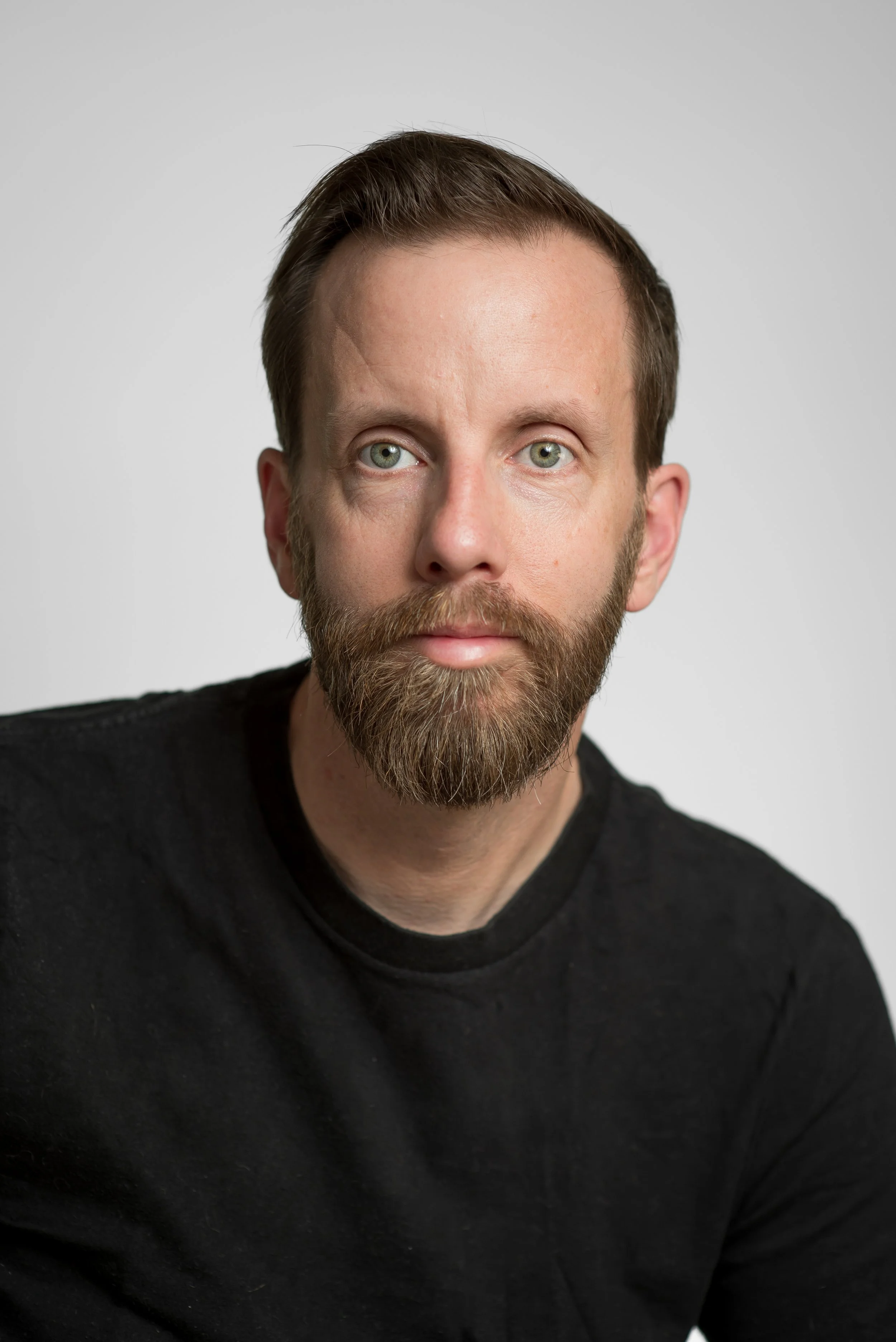 Photo of Tyler Sneezby. He has light skin, short brown hair, blue eyes, and a short brown beard. He is wearing a black long sleeve shirt and looking at the camera.